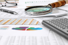 Pen, eyeglasses, calculator and magnifying glass on financial reports