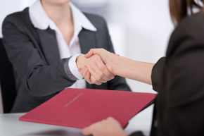 Businesswomen shaking hands and exchanging a folder