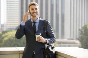 Businessman standing outside the office on the phone with coffee