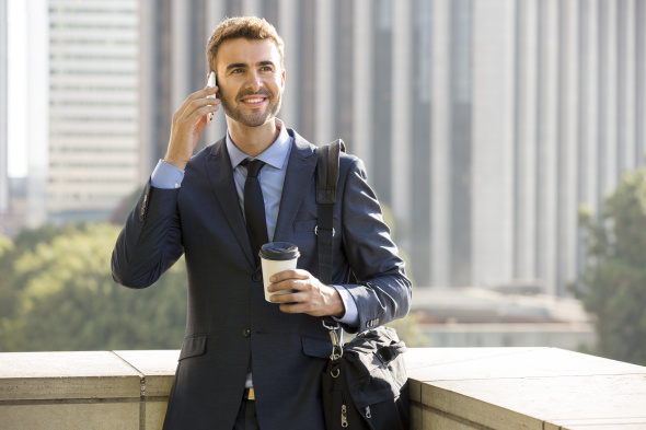 Businessman standing outside the office on the phone with coffee