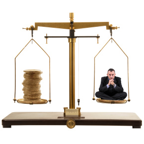Businessman sitting on scales with stack of coins in other tray