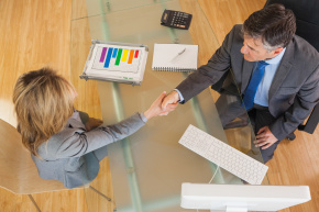 Older businessman shaking hands with businesswoman across desk