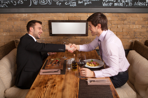 Two businessmen shaking hands at a restaurant table