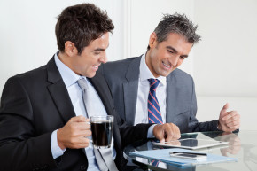 Two happy businessmen looking at digital tablet at desk in office