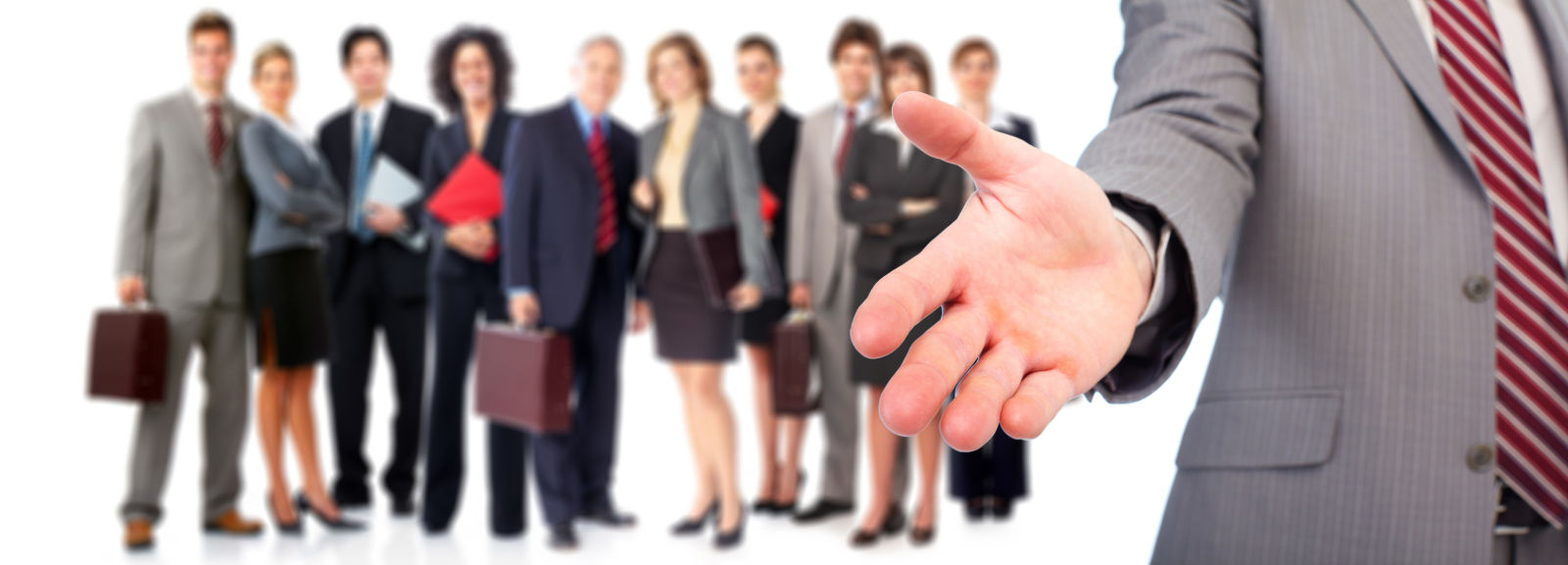 Man in suit with hand extended, coworkers in background