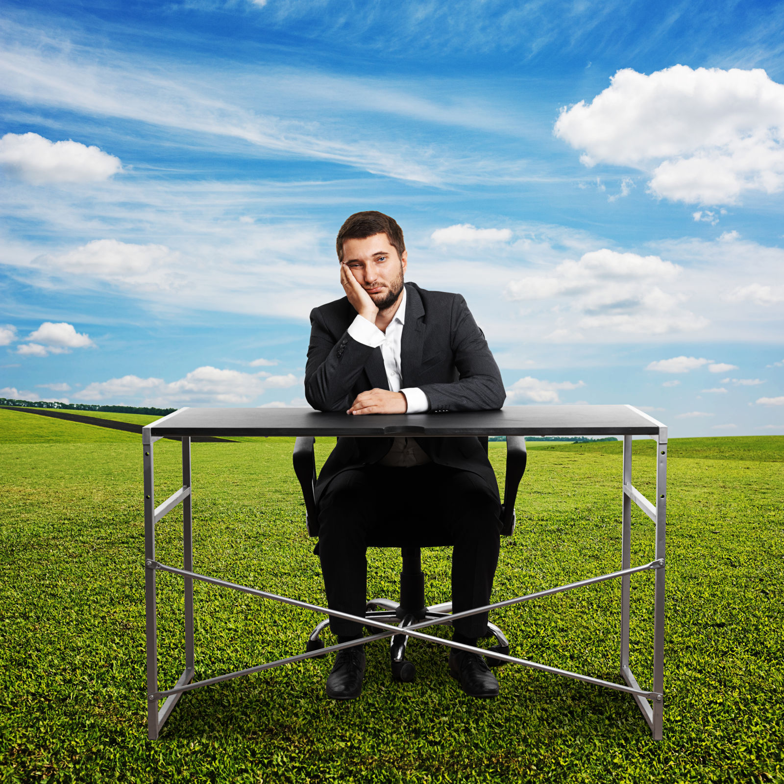 Sad businessman sitting at desk outdoors and looking straight ahead