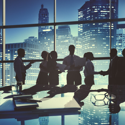 Several businesspeople talking and shaking hands, silhouette against city skyline
