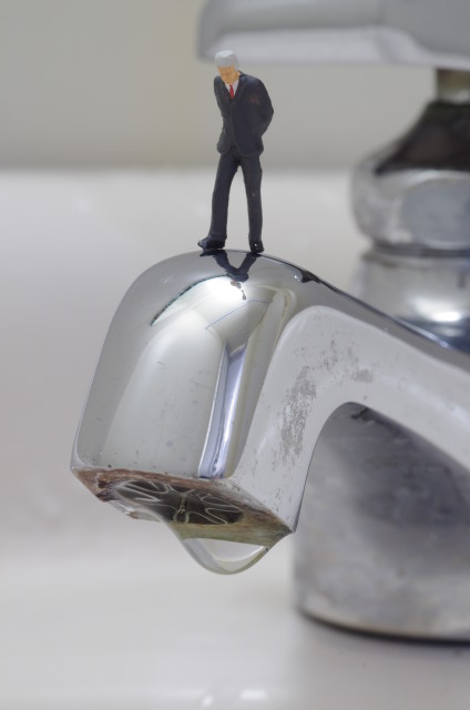 Tiny businessman standing on dripping faucet