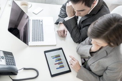 Overhead view of male and female business partners analyzing statistical annual report represented in graphs on digital tablet.