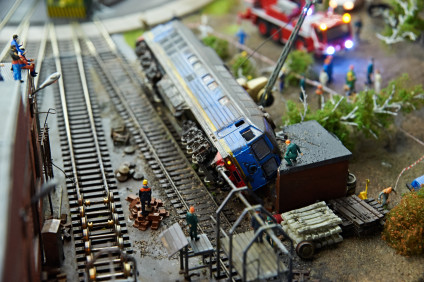 Model train derailed as model workers look on