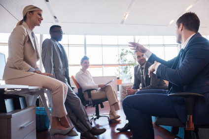Businesswoman sitting on table while talking with four coworkers