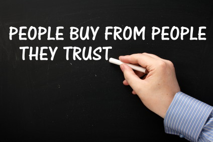 Man's hand writing "People buy from people they trust" on a chalkboard