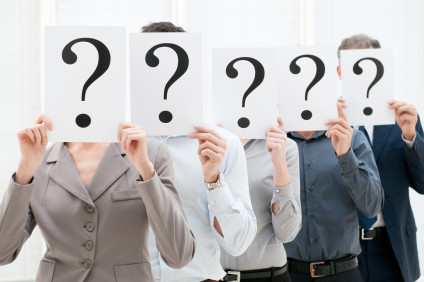 Group of businesspeople hiding their faces behind question mark signs at office