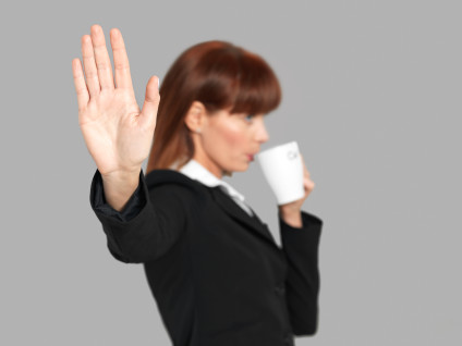 Young businesswoman putting hand out in "stop" gesture while sipping coffee