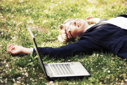 Happy businesswoman with laptop lying on the grass