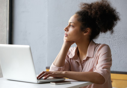 Young black woman sitting in front of laptop looking thoughtful