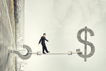 Young businessman walking on bungee cord between question mark and dollar sign