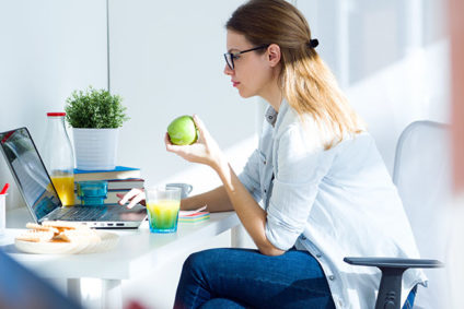 Young woman eating an apple and working on a laptop at home