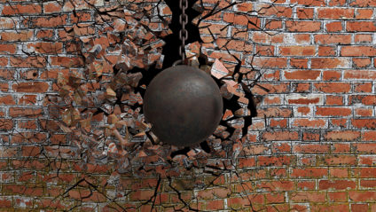 Metallic rusty wrecking ball on chain shattering an old brick wall