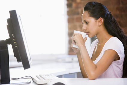Woman drinking coffee in front of desktop computer