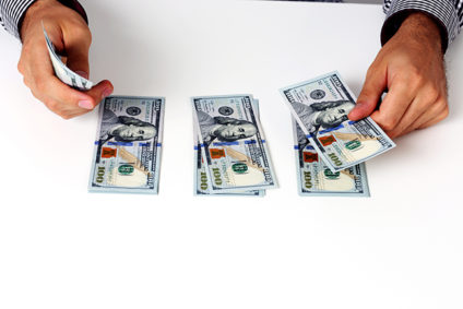 Man counting $100 bills into three piles