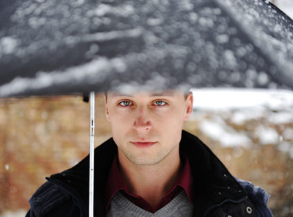 Young man under rain-covered umbrella