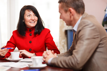 Businesswoman in a meeting with a male colleague smiling at him as they sit at a table discussing paperwork over coffee