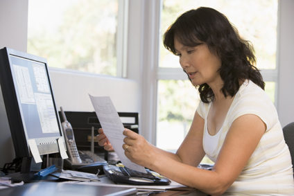 Woman in home office looking at paperwork in front of computer