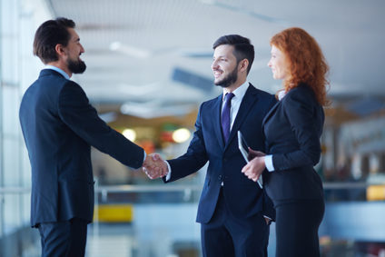 Two men shaking hands as woman stands with one