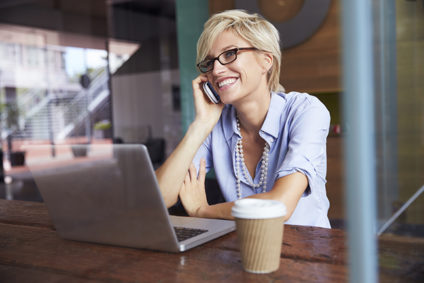 Businesswoman using phone working on laptop in coffee shop
