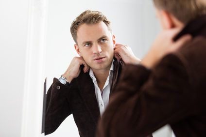 Young man fixing collar in mirror