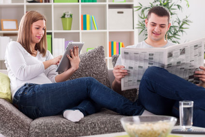 Woman with tablet and man with newspaper reading news at home