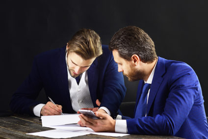 Businessman signing document as another looks on