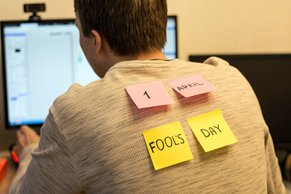 Man at desk with "April fool" stickies on his back