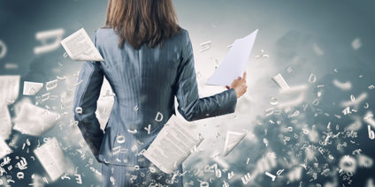 Woman in business attire with papers flying around behind her back